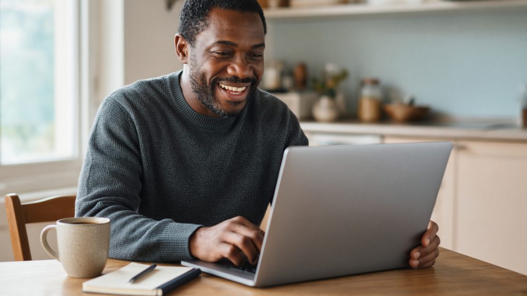 A small business owner writing down a domain name idea beside a laptop