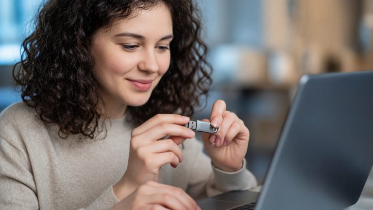 A woman inserting a USB flash drive into the side of a laptop